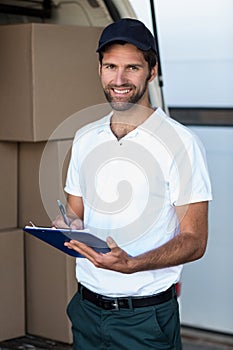 Delivery man writing on clipboard while standing next to his van