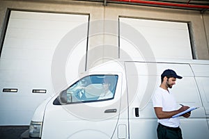 Delivery man writing on clipboard while standing next to his van