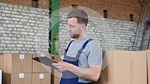 Delivery man writing something to clipboard. Courier checks the parcels on warehouse