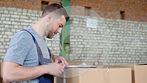 Delivery man writing something to clipboard. Courier checks the parcels on warehouse