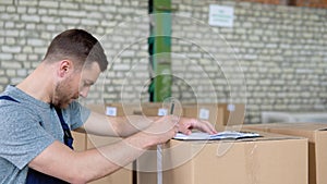 Delivery man writing something to clipboard. Courier checks the parcels on warehouse