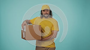 Delivery man in yellow uniform catching and shaking a box, listening to what is inside it, giving out to the camera