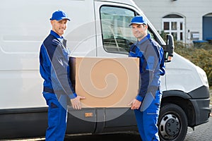 Delivery Men Carrying Cardboard Box Against Truck