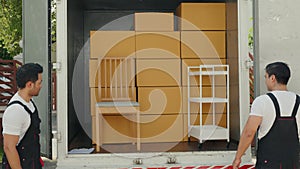 Delivery men unload cardboard boxes from a truck. Movers in uniform work