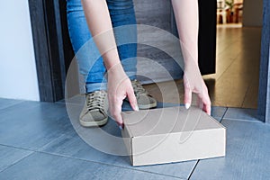 Delivery of parcels to the door. A woman in blue jeans picks up a box with goods delivered by a delivery service from the doorway