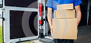 Delivery person holding stack of boxes in front on van background. copy space