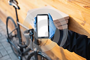Delivery person standing next to a bicycle with pizza boxes holds a phone with whote screen.