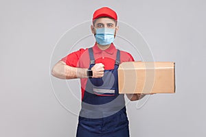 Delivery on quarantine. Ontime service! man with surgical medical mask in blue uniform and red t-shirt standing, holding delivery