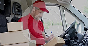 Delivery service man sitting in van and writing documents on clipboard before delivering a package to customer