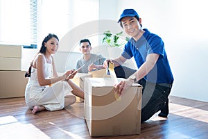 Delivery service worker man in blue uniform help happy couple customer packing parcel with tape in customer home.Woman with tablet