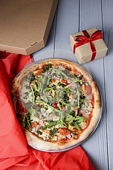 Delivery traditional Italian pizza top view for promotions and discounts with a small present box over wooden background
