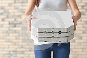 Delivery woman with cardboard pizza boxes on brick wall background