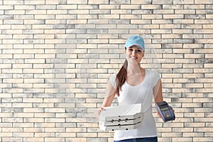 Delivery woman with cardboard pizza boxes and payment terminal on brick wall background