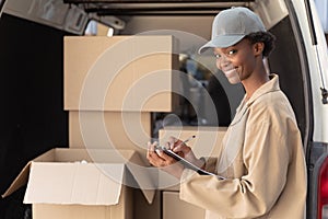 Delivery woman looking at camera while writing on clipboard near van outside the warehouse