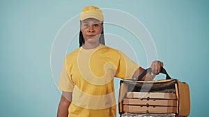 Delivery woman in uniform holding open portable refrigerator backpack with pizza boxes. Isolated on blue background.