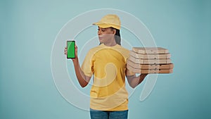 Delivery woman in uniform holding pizza boxes and smartphone, looking at the screen. Advertising area, workspace mockup.