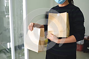 Delivery woman wearing protective face mask coronavirus and hand holding craft paper food packaging bag service, Postman express