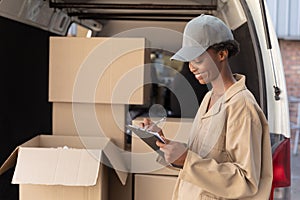 Delivery woman writing on clipboard near van outside the warehouse