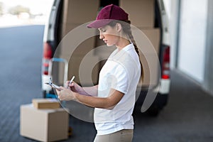 Delivery woman writing on clipboard while standing next to van