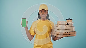 Delivery woman in yellow uniform holding pizza boxes, coffee and smartphone. Advertising area, workspace mockup.