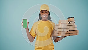 Delivery woman in yellow uniform holding pizza boxes, coffee and smartphone, smiling at the camera. Advertising area