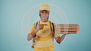 Delivery woman in yellow uniform holding pizza boxes and pointing at it. Isolated on blue background.