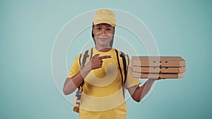 Delivery woman in yellow uniform holding pizza boxes and shows a thumbs up gesture. Isolated on blue background.