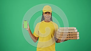 Delivery woman in yellow uniform holding pizza boxes and smartphone. Isolated on green background. Advertising area
