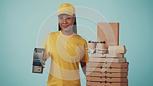 Delivery woman in yellow uniform holding portable payment terminal, looking at coffee cups and pizza boxes. Isolated on