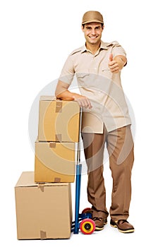 Deliveryman Gesturing Thumbs Up By Stacked Cardboard Boxes
