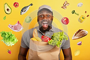 Deliveryman with happy expression ready to deliver bag with food. Yellow background.