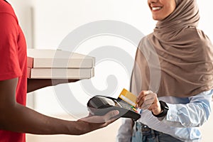 Deliveryman holding POS machine, muslim woman paying with card