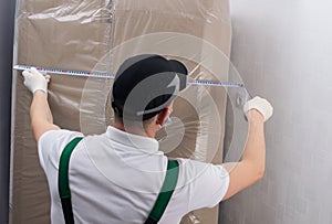 The deliveryman measures the dimensions of the box to clarify the dimensions of the doorway