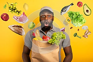 Deliveryman with wondered expression ready to deliver bag with food. Yellow background.