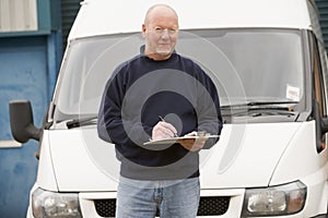 Deliveryperson standing with van and writing