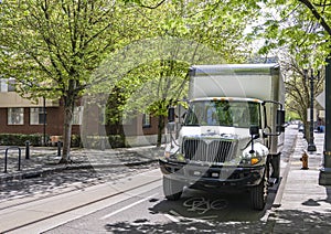 In demand white middle duty rig semi truck with day cab and box trailer for local delivery standing on the urban city street with