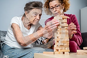 Dementia therapy. Social worker and dog plays an educational board game with senor patient at nursing home. Jenga game. Caregiver