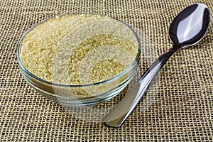 Demerara sugar in glass bowl with spoon beside on jute fabric