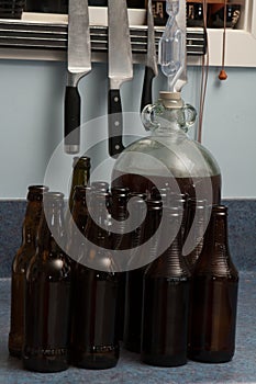 Demijohn fulled of fermented beer with airlock and dark brown bottles