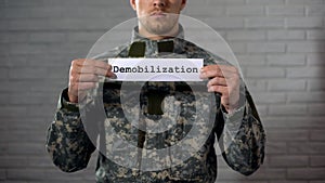 Demobilization word written on sign in hands of male soldier, end of term