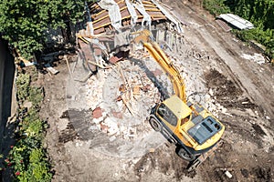 Demolition of building aerial view from drone. Excavator breaks old house