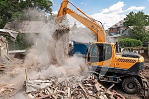 Demolition of building by industrial excavator. Bucket breaks walls and roof of old house full of dust