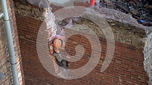 Demolition of old abandoned house, workman in orange helmet destroy wall with jackhammer. Deconstruction of living house