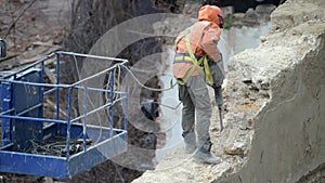 Demolition of old abandoned house, workman in orange helmet destroy wall with jackhammer. Deconstruction of living house