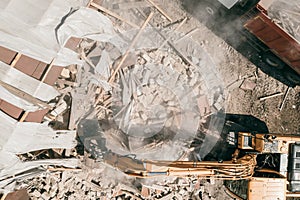 Demolition of old house building for new construction by excavator bucket, aerial top view