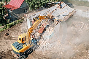 Demolition of old house building for new construction by excavator bucket, aerial view. City development