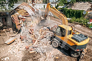 Demolition of old house building for new construction by excavator bucket, aerial view. City development