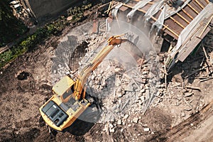 Demolition of old house building for new construction by excavator bucket, aerial view. City development