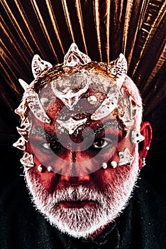 Demon head with thorns on face appearing from darkness, underworld concept. Evil monster with red skin wearing metallic photo
