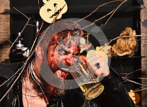 Demon with horns and evil smile face drinks ale. Halloween party concept. Man wearing scary makeup holds beer